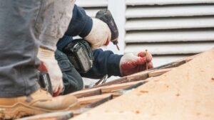 Roofer in work gloves using a cordless drill on a roof